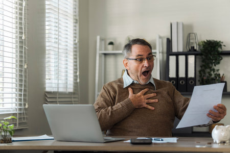An elderly man celebrates while reviewing retirement savings documents and annual tax audit.の写真素材