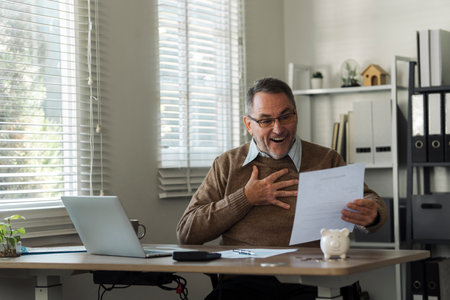 An elderly man celebrates while reviewing retirement savings documents and annual tax audit.の写真素材