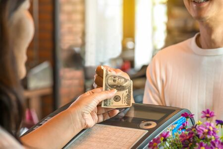Young man paying cash at register counter .Customer and woman cashier holding money with smiling face, bokeh blurred background,business concept.の写真素材
