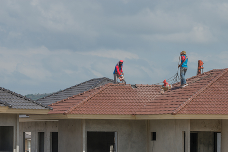 Skillful workers tiling on rooftop of a new house.
Professional roof builder with safety equipment finishing roof tiling for a new property project.の写真素材