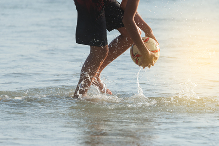 Boy picking a ball up from the sea at sunset.
Beach football ,family activity during wonderful vacation at tropical beach.の写真素材