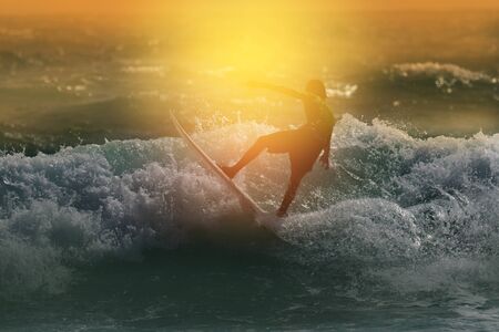 Silhouette surfing at sunset.Happy surfer enjoy big wave during vacation at tropical beach.