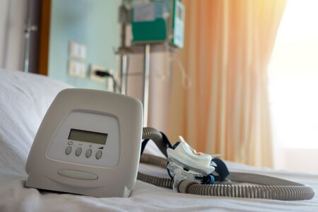 CPAP machine mask and tube on white bed cover on bed of hospital with blurred   curtain background.  CPAP machine components.Obstructive sleep apnea therapy.の写真素材