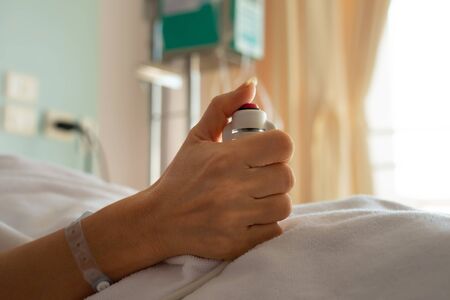 Woman patient  in hospital dress under white blanket holding red emergency call button while lying in  bed.Hand holding  nurse call button,selective focused.の写真素材