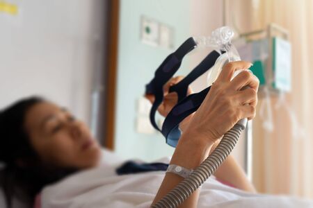 Senior patient woman hands holding Cpap mask  lying  in hospital room.Obstructive sleep apnea therapy.の写真素材