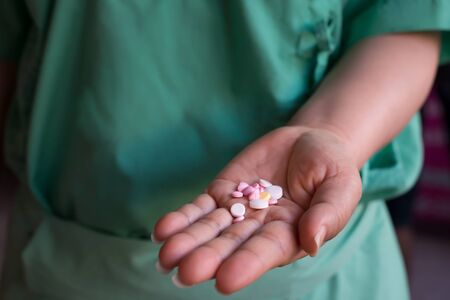 Close up of woman swelling hand holding lot of pills wearing hospital green clothes.Pills on woman left hand.の写真素材
