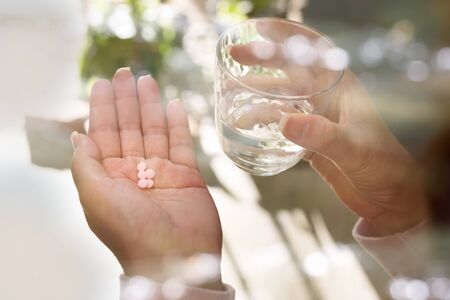 Close up of woman hands holding lot of pills and glass of water with bokeh and blur background, back angle view.Pills on woman hand.の写真素材