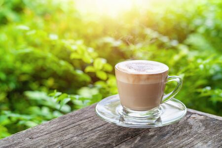 Hot coffee cappuccino in the morning on wooden with green background leavesの写真素材