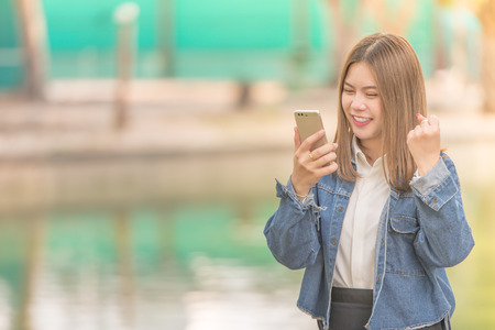 Success and Surprised young Asian woman using smart phone outdoors.Girl happy She was glad to get good newsの写真素材
