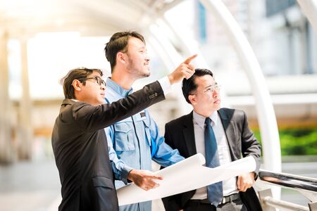 engineers meeting at terrace on top of construction site. Coworkers discussing. Boss and worker argue. Conversation in team.wear helmet hold paper plansの写真素材