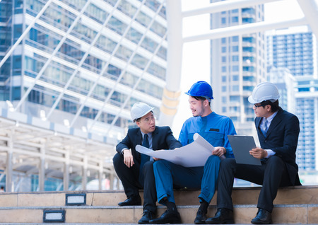 Business engineer planing with white helmet and holding drawing paper in hand against city...