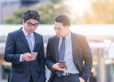 Half length of two young bearded modern businessman using smart phone handhold looking downward the screen - technology, business, work conceptの写真素材