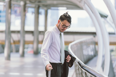 Businessman calling on cell phone while pulling baggage and walking in outdoor covered walkway, panoramic banner with copy spaceの写真素材