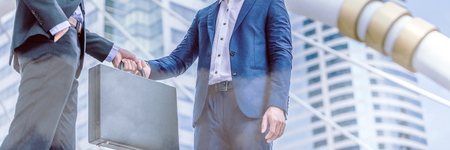 Businessman transfer deal, business black briefcase exchange urban city background.handover of a suitcase in the hands of partners.の写真素材