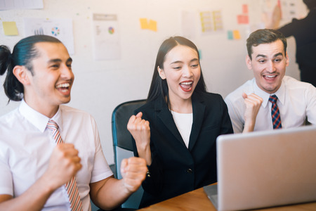 Happy business people celebrate success looking at laptop screen in the office. Successful corporate team of partners and coworkers, winners excited of victoryの写真素材
