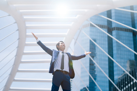 Celebrating success. Low angle view of excited young businessman keeping arms raised and expressing positive while standing outdoors with office building in the backgroundの写真素材