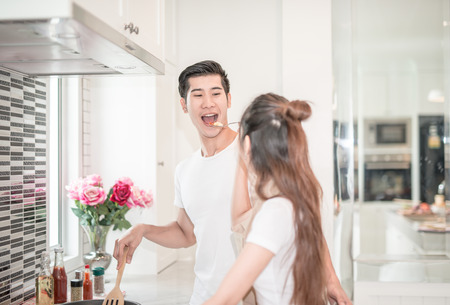 young Asian woman having her husband tasting pasta dish .happy couple in kitchenの写真素材