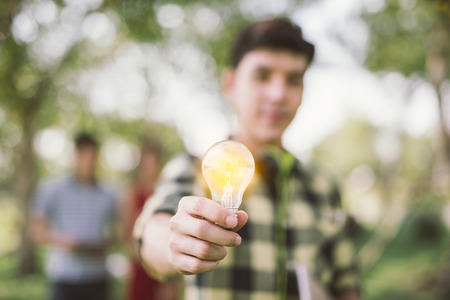 Man teen student holding to the illuminated bulb . Light Bulb Think Ideas Create .focus Light Bulbの写真素材