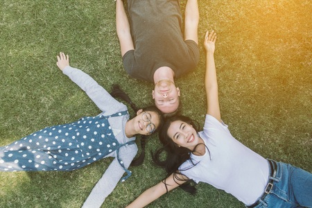 Young family with daughter laying in the park on the green grass and looking at the camera, top view.の写真素材
