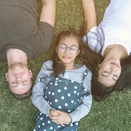 Young family with daughter laying in the park on the green grass and looking at the camera, top view.の写真素材