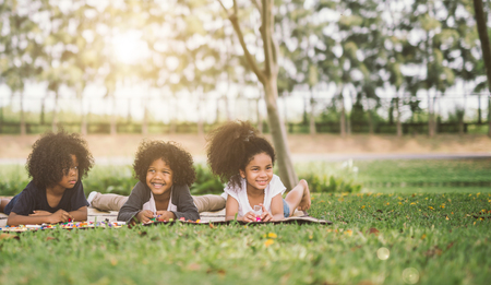 Happy three little friends laying on the grass in the park. american african children playing Lego in parkの写真素材