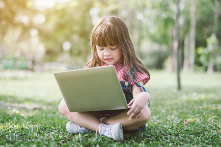 Little girl with laptop. happy children in nature technology education conceptの写真素材