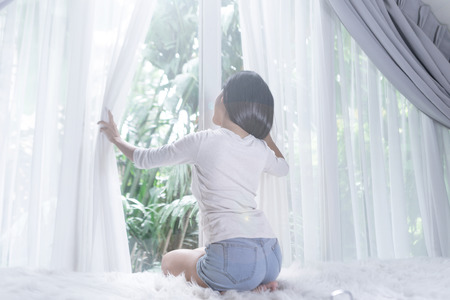 young woman in modern house opening window curtains after wake upの写真素材