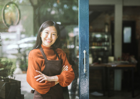 Beautiful asian woman store owner with standing in the doorway of her coffee shop looking at camera...