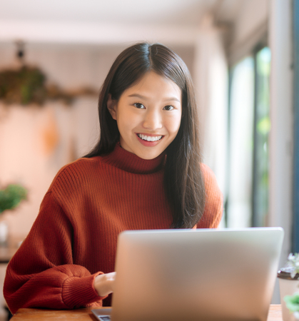 Happy young Asian girl working at a coffee shop with a laptop looking at camera.の写真素材