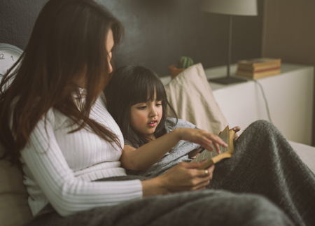 mother and daughter reading book at home in the bedroom