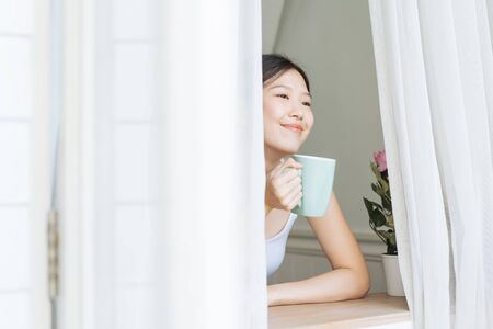 Portrait Asian woman relaxing on wooden chair with coffee at home