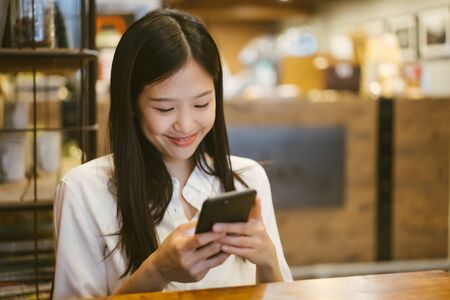 Young Asian woman using phone at a coffee shop happy and smile.の写真素材