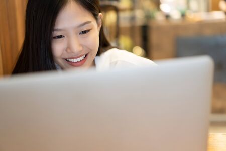 Happy young Asian woman using phone and working with a laptop in the coffee shop cafe office.の写真素材