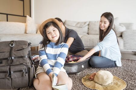 Happy Asian family is preparing for travel at home .Mom daughter and father are packing suitcases for the trip.の写真素材