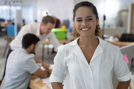 Portrait of successful young African businesswomanÂ at office, colleagues in background.