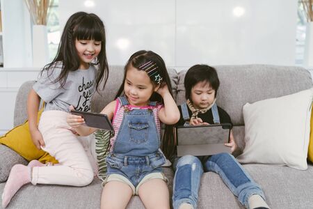 group of little children watching film movie cartoon together on digital tablet and phone. Kids playing with smartphone with friends at home.の写真素材