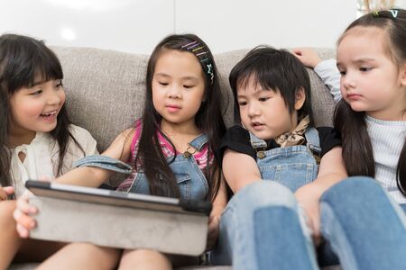group of little children watching film movie cartoon together on digital tablet. Kids playing with tablet with friends at home.の写真素材