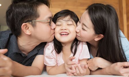 Asian Parents kissing their little daughter on both cheeks. family portrait.の写真素材