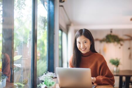 Happy young Asian girl working at a coffee shop with a laptop looking at camera.の写真素材