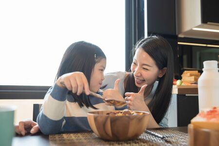 mom and daughter eating Cereals with milk having breakfast in kitchen.の写真素材