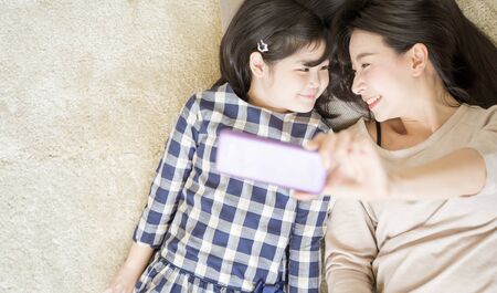Mother is selfie with her little daughter using a smart phone camera while eye contact with daughter...