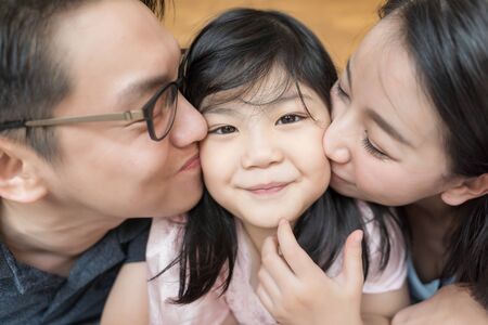 Asian Parents kissing their little daughter on both cheeks. family portrait.の写真素材