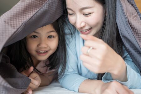 Mother and her daughter child girl playing in the bedroom and putting blanket on . Happy Asian familyの写真素材