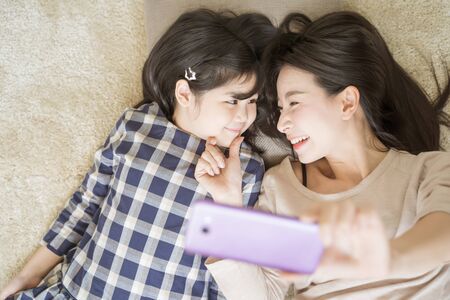 Mother is selfie with her little daughter using a smart phone camera while eye contact with daughter .Asian family conceptの写真素材