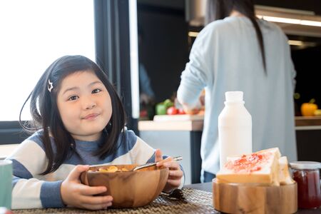 mom and daughter eating Cereals with milk having breakfast in kitchen.の写真素材