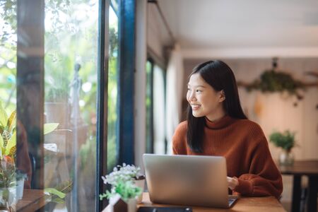 Happy young Asian girl working at a coffee shop with a laptop.の写真素材