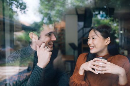 Couple having coffee on a date talking and smile together. shot through window glassの写真素材