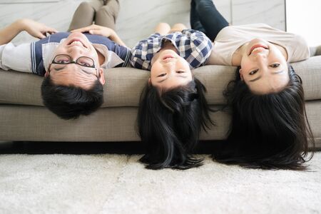 Portrait Happy Asian Family hanging upside down on sofa in living roomの写真素材