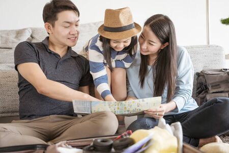 Happy Asian family is preparing for travel at home .Mom daughter and father are packing suitcases for the trip.の写真素材