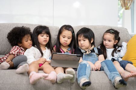 group of little children watching film movie cartoon together on digital tablet. Kids playing with tablet with friends at homeの写真素材